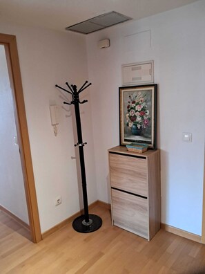 Ein Zimmer mit Kleiderständer, einem an der Kommode hängenden Blumenbild und einer Tür.