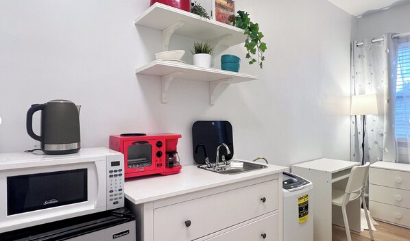 A compact kitchenette with a microwave, toaster, kettle, and sink.