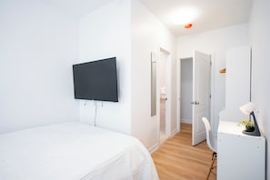 A bedroom with a bed, a TV mounted on the wall, a desk with a chair, and a door leading to another room. - Budget Stylish Suite! Kitchenette! Washer! Parking (Queens)