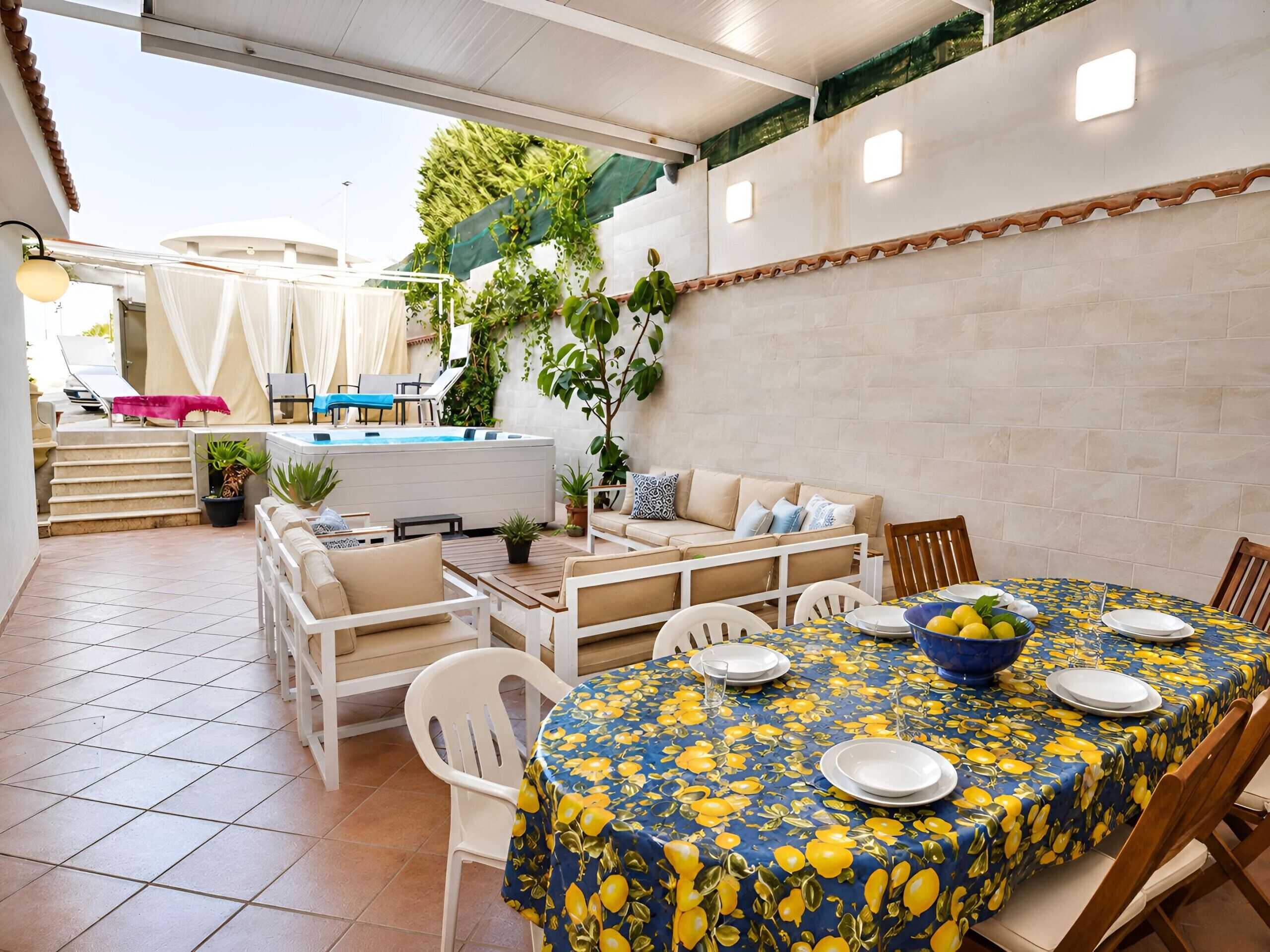 Un área de comedor al aire libre techada, con piscina, sofá y plantas en macetas.