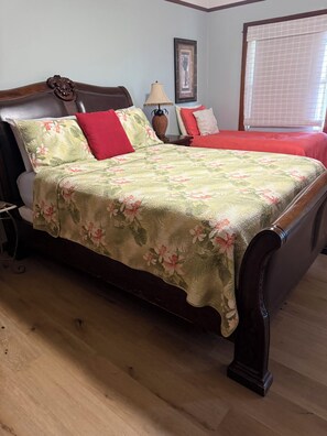 Ein Bett mit floralem Überwurf, einem roten Kissen und einem Holz-Kopfteil.