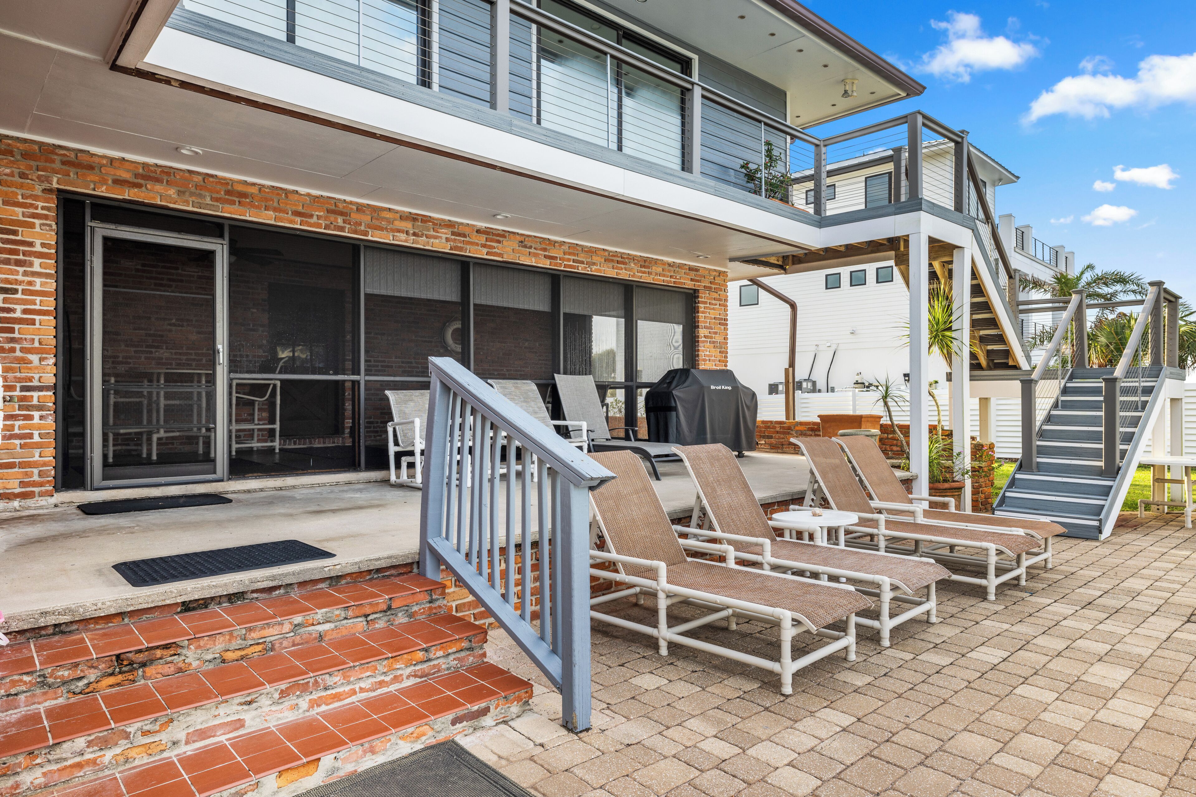 Une maison moderne à deux étages dotée d’un patio aménagé avec des meubles d’extérieur et un barbecue.