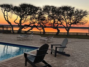 Ein Poolbereich mit Liegestühlen und Blick auf einen Sonnenuntergang über dem Wasser.