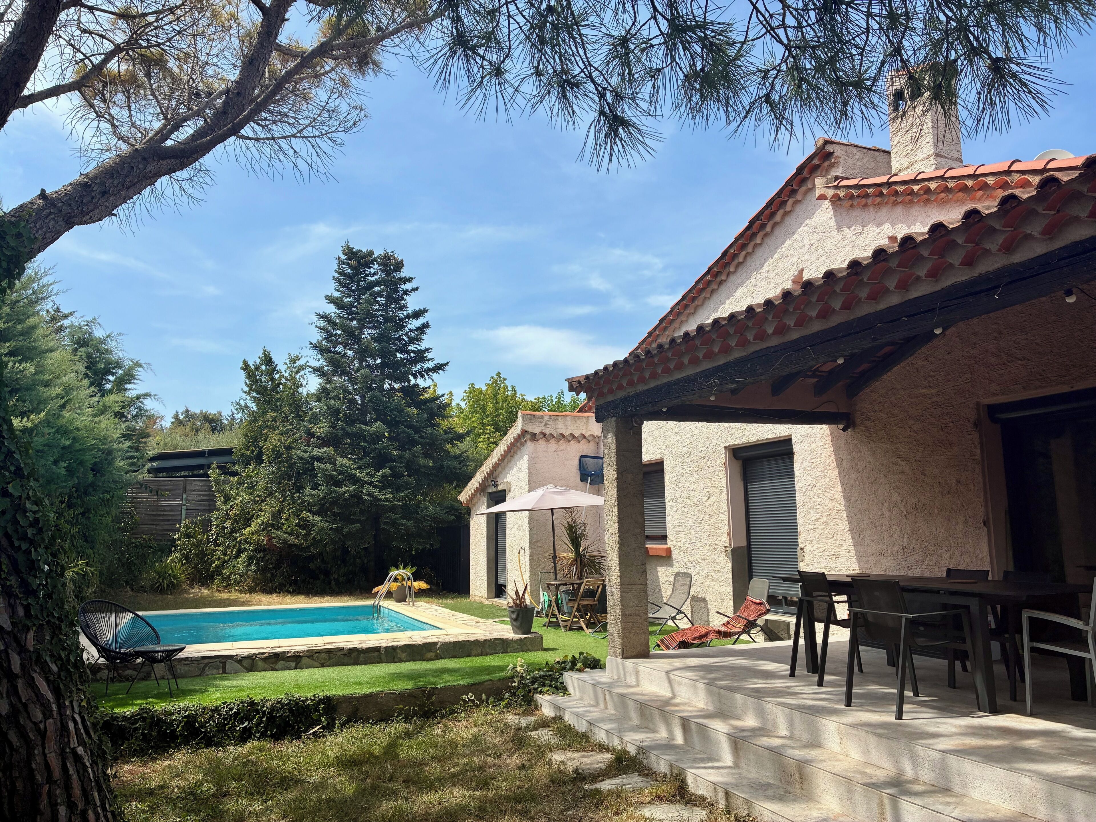 A pool area with a patio, outdoor furniture, and a building with a tiled roof.