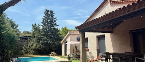 A pool area with a patio, outdoor furniture, and a building with a tiled roof.