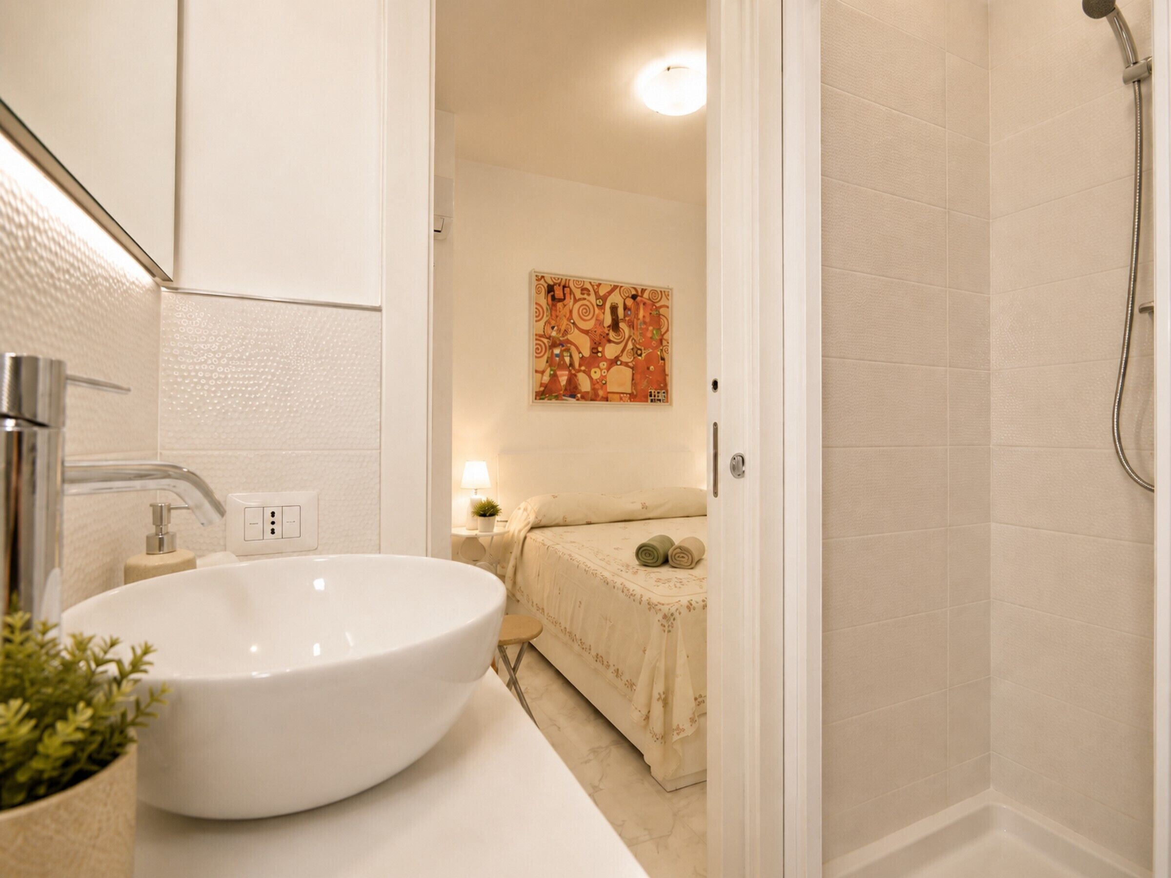 Een badkamer met een witte wastafel, een douche en een bed met een bloemenprint.