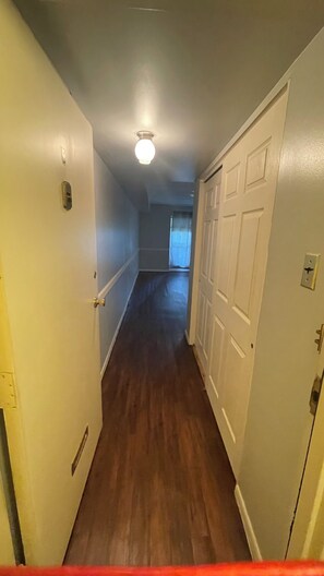 A hallway with wooden flooring, white walls, and a ceiling light.