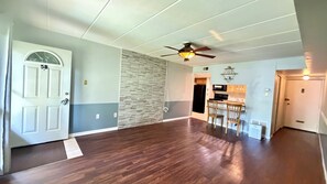 A spacious room with a wooden floor, a ceiling fan, and a kitchen area with a dining table and chairs.