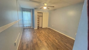 A hallway with wooden flooring, a ceiling fan, and a door leading to a closet.