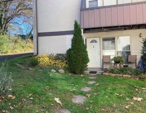 A residential building with a front porch, a small tree, and a pathway leading to the entrance.