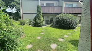 A residential building with a well-maintained lawn, a pathway, and a variety of shrubs and trees.