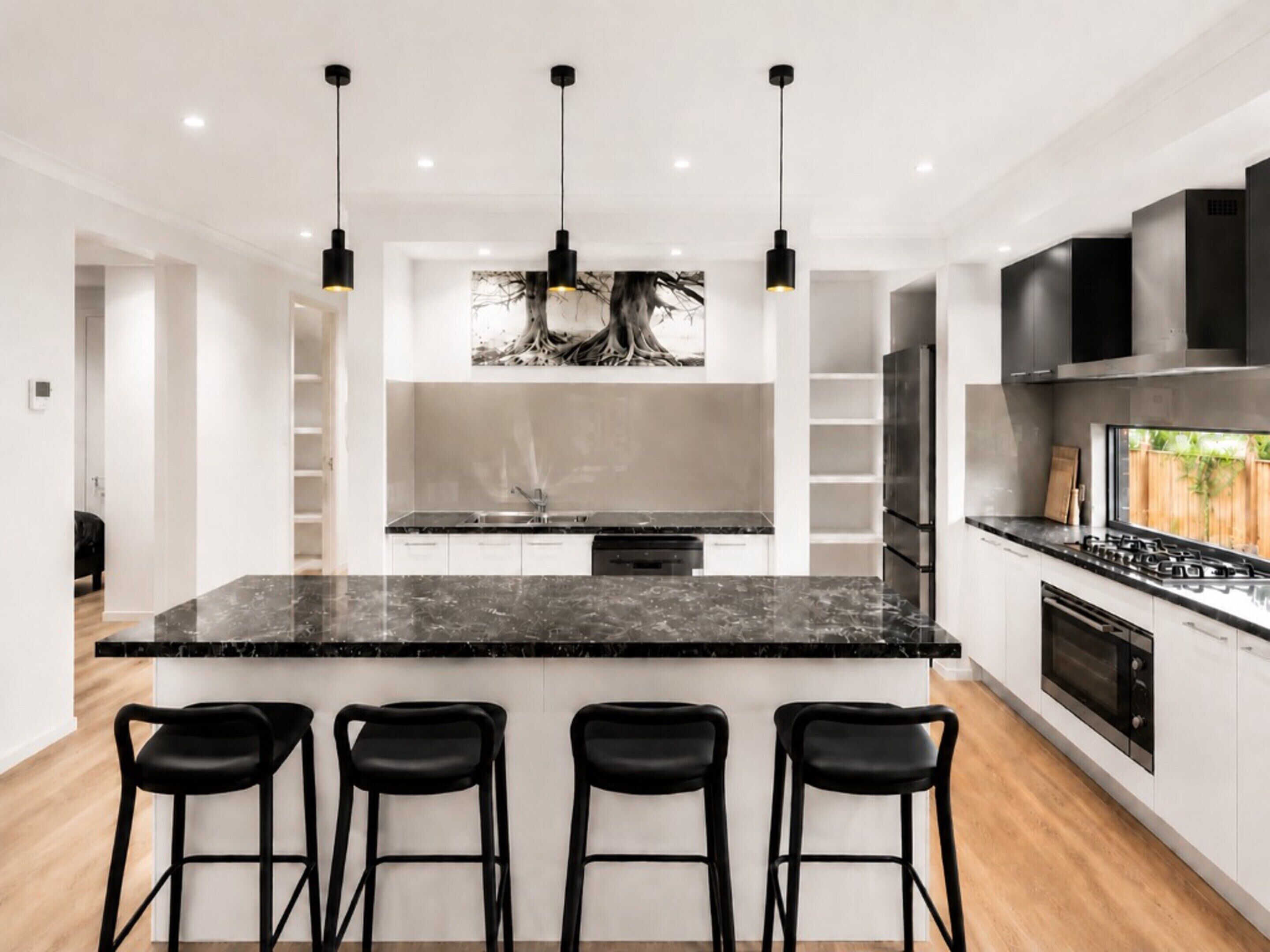 Una cocina moderna con una isla central, taburetes de bar y un ventanal grande.