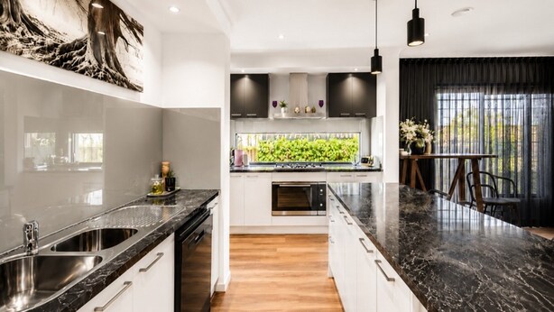 Una cocina moderna con encimera de mármol negro, armarios blancos y horno empotrado.