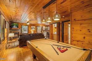 A wooden interior with a pool table, a sofa, and pendant lighting. - Kiss Me in the Smokies (Pigeon Forge)