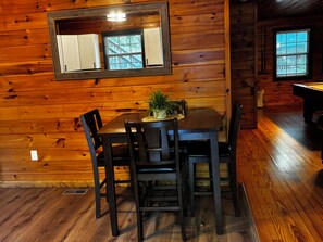 A wooden interior with a dining table and chairs, a potted plant, and a window with a view of a wooden deck. - Kiss Me in the Smokies (Pigeon Forge)