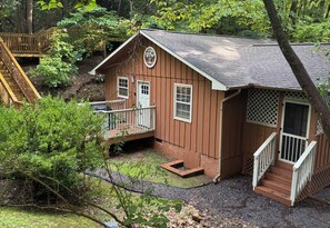 A wooden cabin with a porch, a small deck, and a staircase leading to the entrance. - Kiss Me in the Smokies (Pigeon Forge)