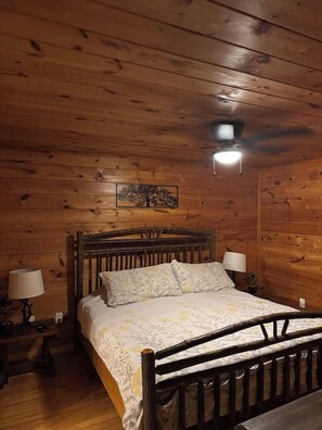 A wooden-paneled room with a bed, two bedside lamps, and a ceiling light fixture. - Kiss Me in the Smokies (Pigeon Forge)