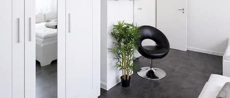 A modern room with a wardrobe, a television, a potted plant, a black chair, and a white bench.