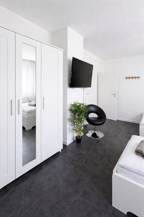 A modern room with a wardrobe, a television, a potted plant, a black chair, and a white bench.