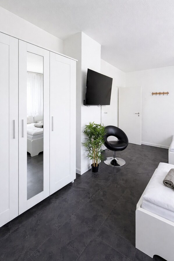 A modern room with a wardrobe, a television, a potted plant, a black chair, and a white bench.