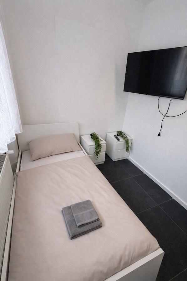 A modern bedroom with a bed, a flat-screen TV mounted on the wall, and two bedside tables with plants.