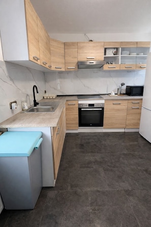 A modern kitchen with wooden cabinets, a built-in oven, a microwave, and a grey floor.