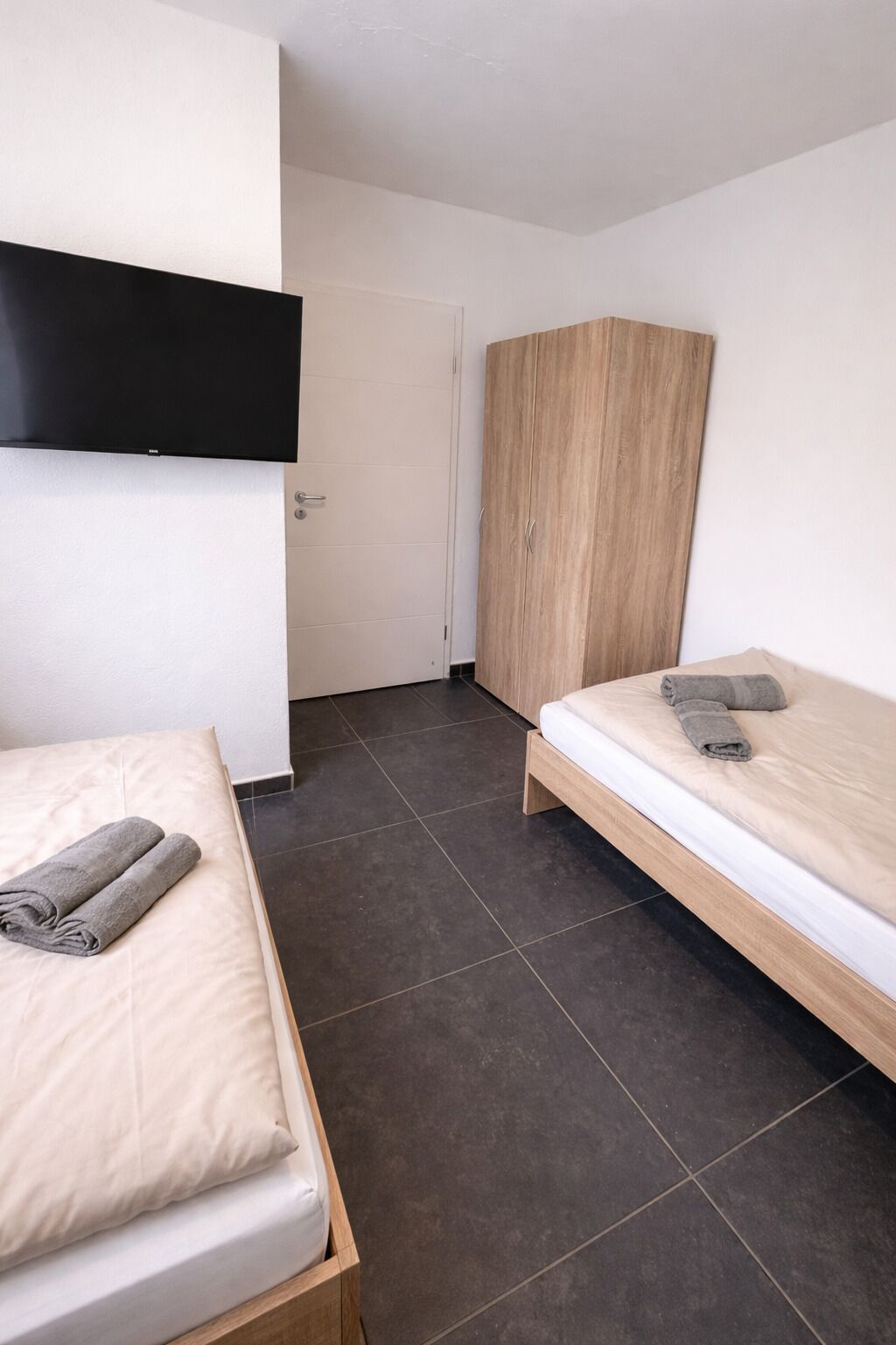 A bedroom with two beds, a wardrobe, and a television mounted on the wall.