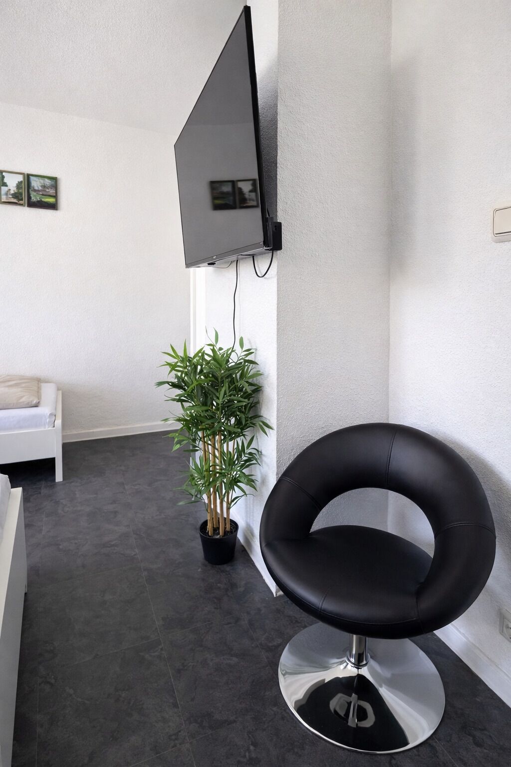 A modern room with a black leather chair, a potted plant, a white sofa, and a mounted flat-screen TV.