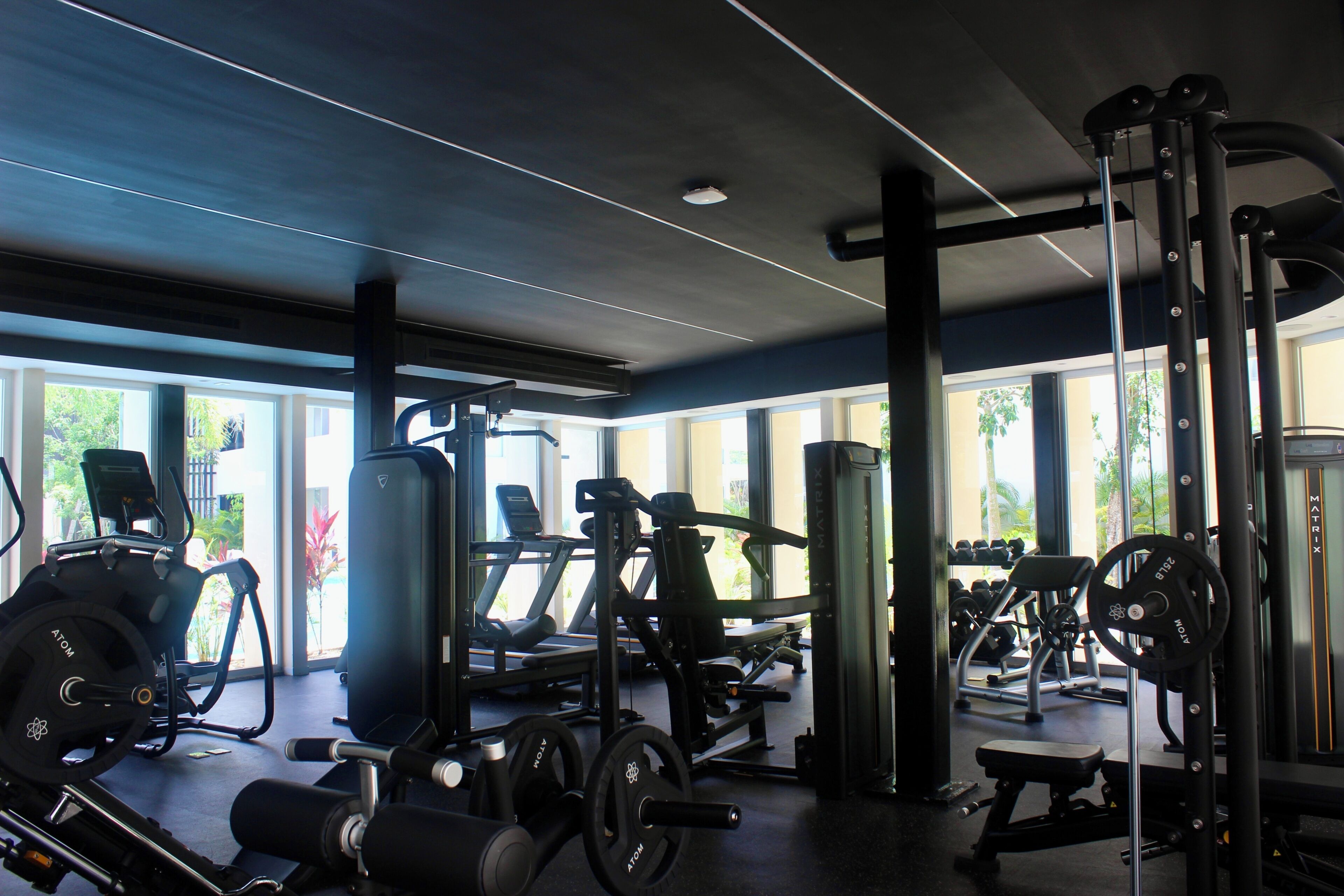 A gym with various exercise equipment, large windows, and a ceiling with linear lighting.