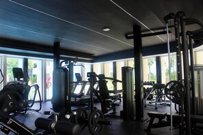 Ein Fitnessraum mit verschiedenen Trainingsgeräten, großen Fenstern und einer Decke mit linearer Beleuchtung.