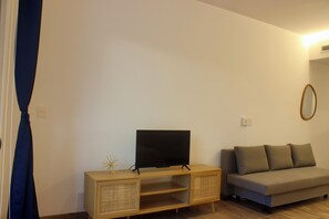 A living room with a TV on a wooden cabinet, a sofa, and a wall-mounted mirror. - Brand-New Studio with 4 Pool Access at The Leaf Playacar, | All-Inclusive (Playa del Carmen)