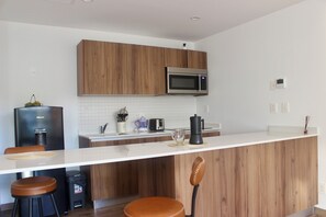 A modern kitchen with wooden cabinets, a stainless steel microwave, a coffee maker, and a trash bin. - Brand-New Studio with 4 Pool Access at The Leaf Playacar, | All-Inclusive (Playa del Carmen)
