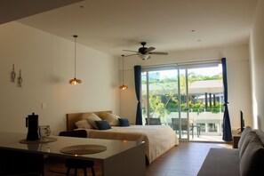 Een moderne hotelkamer met een bed, een zithoek, een bank en een balkon met uitzicht op groen.