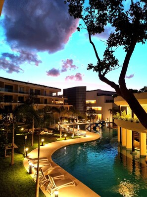 A resort pool area with lounge chairs, a swimming pool, and a building with multiple floors. - Brand-New Studio with 4 Pool Access at The Leaf Playacar, | All-Inclusive (Playa del Carmen)