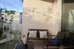 Ein Balkon mit einer Couch und einem Sessel, eine Vase mit Blumen und Blick auf ein Gebäude sowie Bäume.