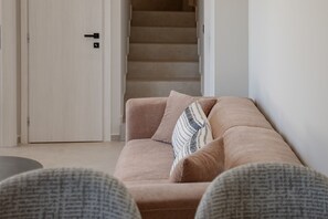 Ein Wohnzimmer mit einem beigefarbenen Sofa, einem gemusterten Zierkissen und einer Treppe im Hintergrund.