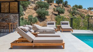 A poolside area with sun loungers and a stone wall. - Metatulia Villa 6 – Private Pool, Jacuzzi & Views (Plakias)
