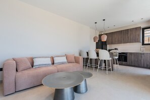 Ein modernes Wohnzimmer mit einer Couch, zwei runden Tischen und einer Küchenzeile mit Barhocker.