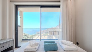 A hotel room with a large bed, two towels, a nightstand, and a view of a mountainous landscape through a sliding glass door. - Metatulia Villa 6 – Private Pool, Jacuzzi & Views (Plakias)