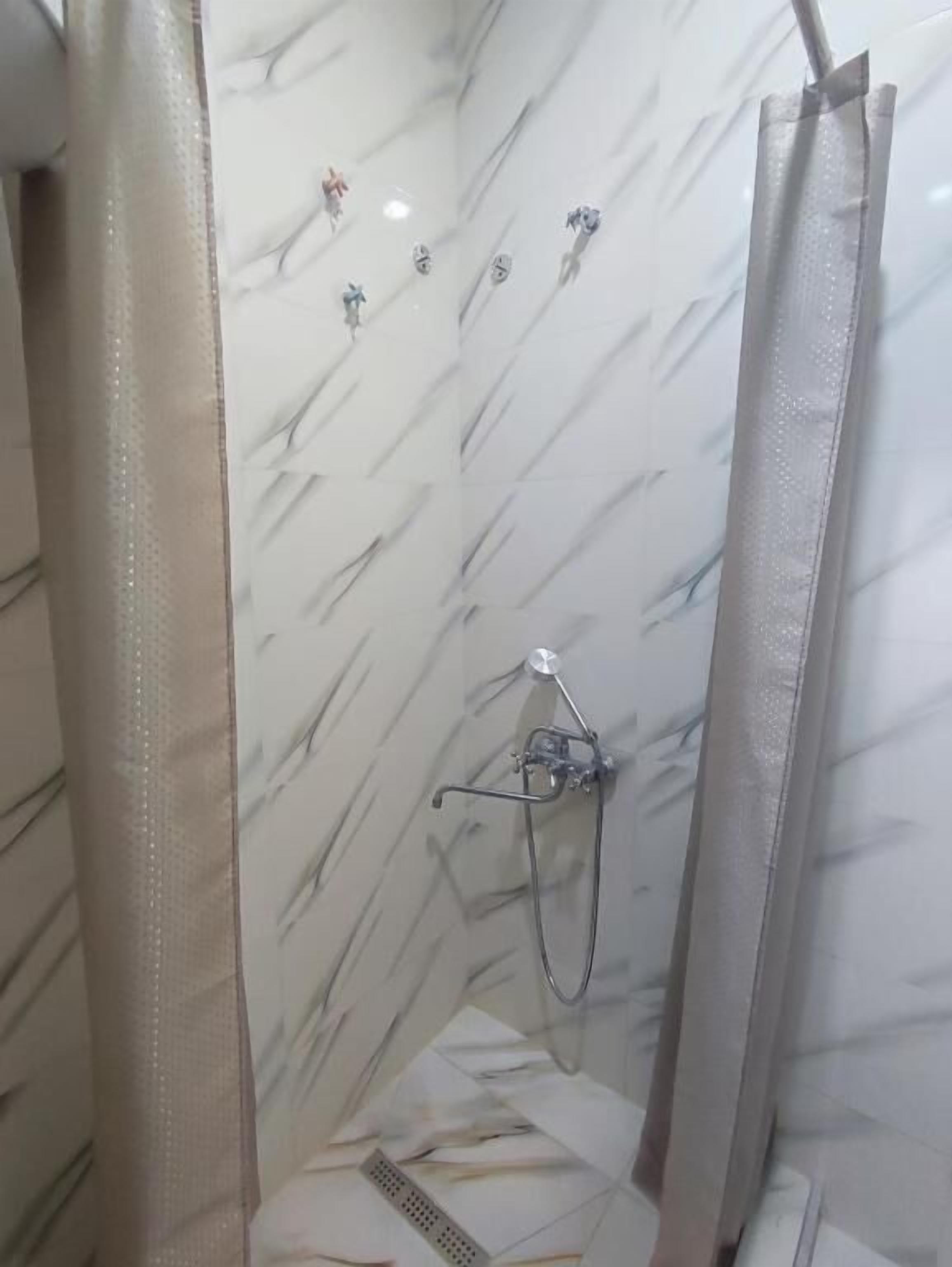 A shower with a marble wall, a showerhead, and a curtain.