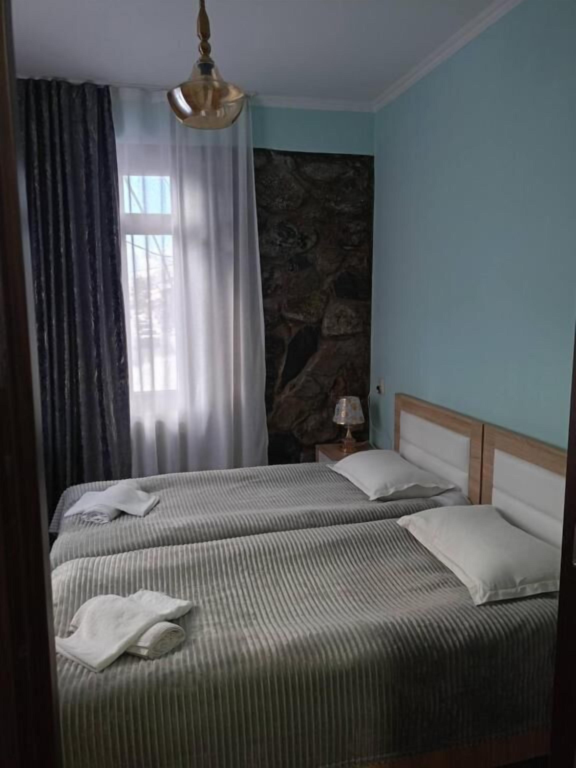 A bedroom with two beds, a stone wall, a window with curtains, and a hanging light fixture.