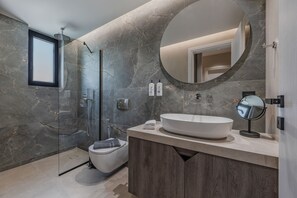 Ein modernes Badezimmer mit einem großen, ovalen Waschbecken, einer Duschkabine aus Glas und einem runden Spiegel.
