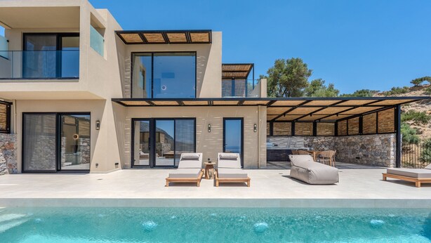 Uma casa moderna de dois andares com piscina, área de estar externa e um muro de pedra.