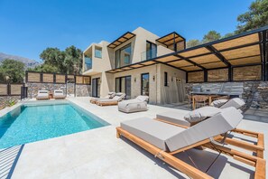 Ein modernes Haus mit Swimmingpool, Sitzgelegenheit im Freien und einer Steinmauer.