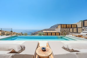 Blick auf ein Schwimmbecken mit Liegestühlen und Meer.