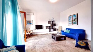 A living room with a blue sofa, a coffee table, a TV, and a bookshelf. - La Finestra sul Mare (Alcamo)