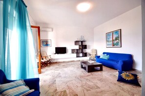 A living room with a blue sofa, a coffee table, a TV, and a bookshelf. - La Finestra sul Mare (Alcamo)