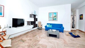 A living room with a blue sofa, a television, a coffee table, and a decorative wall piece. - La Finestra sul Mare (Alcamo)