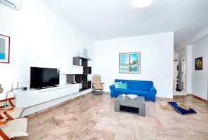 A living room with a blue sofa, a television, a coffee table, and a decorative wall piece. - La Finestra sul Mare (Alcamo)
