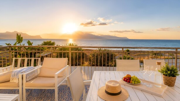 A terrace with white furniture, a table with fruit and glasses, and a view of the ocean at sunset. - La Finestra sul Mare (Alcamo)